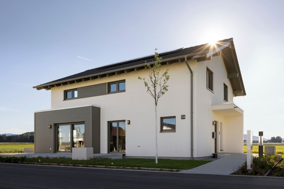 FingerHaus ARTIS 400 Musterhaus im Schwarzwald mit Satteldach, Photovoltaikanlage, weißer Fassade und Holz-Erker, aufgenommen bei Sonnenschein.