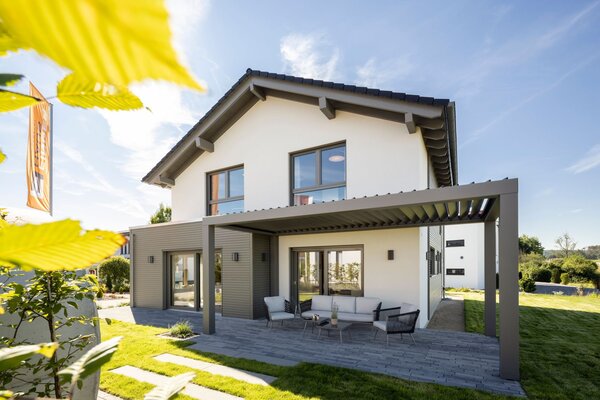 Modernes FingerHaus-Musterhaus ARTIS 300 in Nürnberg mit überdachter Terrasse, großer Glasfront und gepflegtem Garten im Sonnenlicht.