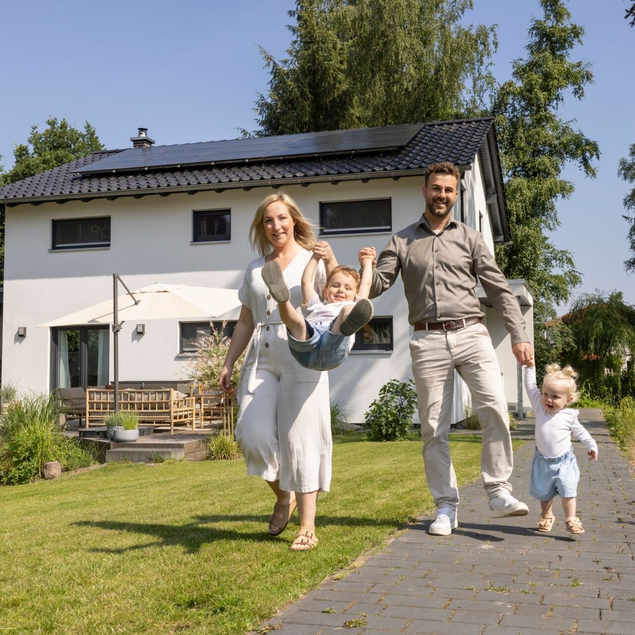 Familie mit zwei kleinen Kindern spielt fröhlich im Garten ihres frei geplanten FingerHaus. Im Hintergrund ist das moderne Einfamilienhaus mit Terrasse zu sehen.