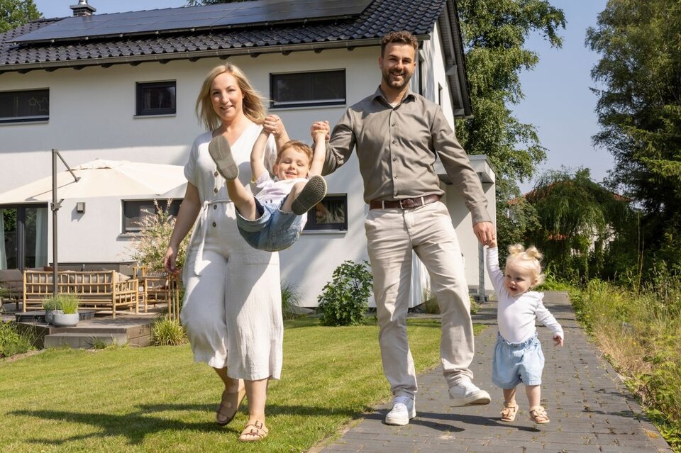Familie mit zwei kleinen Kindern spielt fröhlich im Garten ihres frei geplanten FingerHaus. Im Hintergrund ist das moderne Einfamilienhaus mit Terrasse zu sehen.