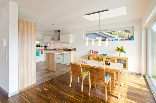 Helle Wohnküche in einem frei geplanten Finger-Haus mit Essbereich, großem Holztisch, moderner Küchenzeile, Kochinsel und bodentiefen Fenstern mit viel Tageslicht.