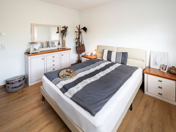 Schlafzimmer eines frei geplanten Kundenhauses mit Doppelbett, Nachttischen und Kommode.