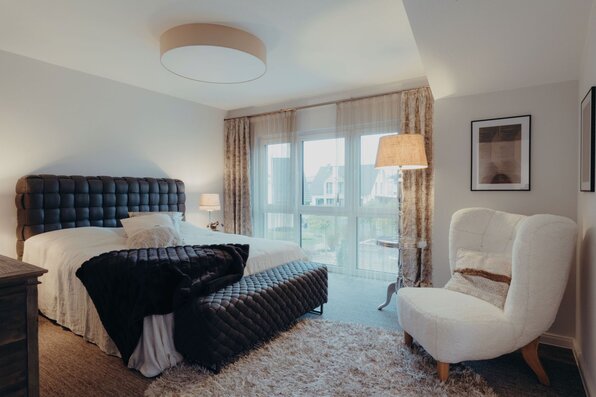 Gemütliches Schlafzimmer mit großem Bett, gesteppter Bank und Sessel im Musterhaus SENTO 503 in Bad Vilbel.