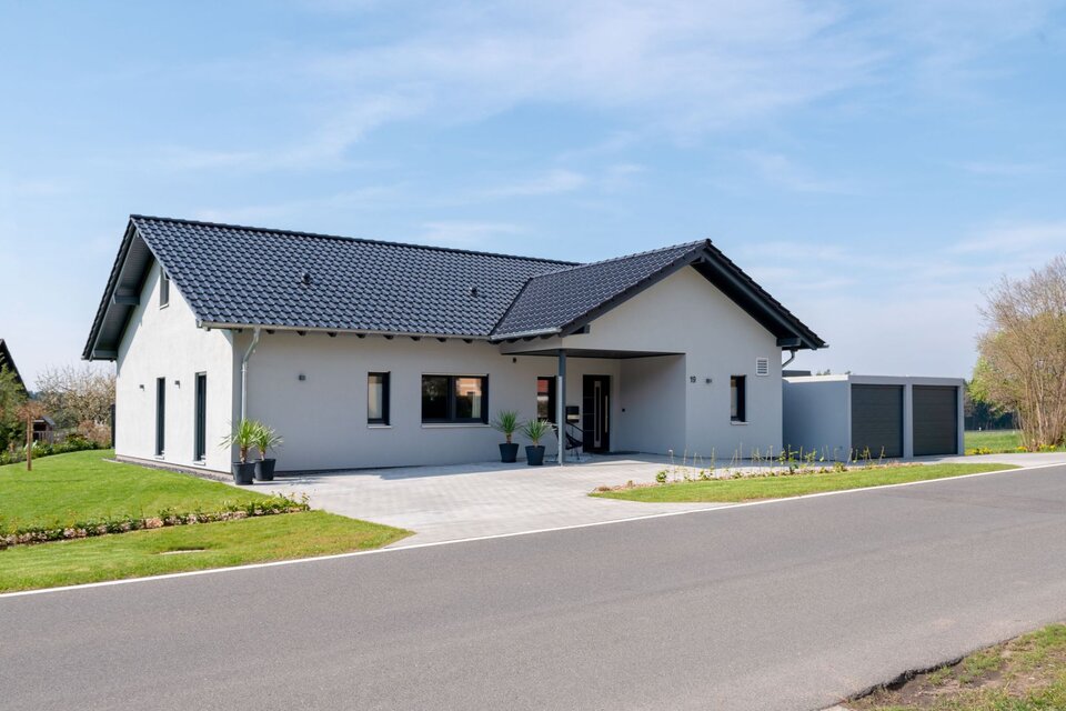 Modernes FingerHaus NIVO 130 mit Satteldach, heller Fassade, überdachtem Eingang und angebauter Doppelgarage, aufgenommen aus Straßenperspektive bei sonnigem Wetter.