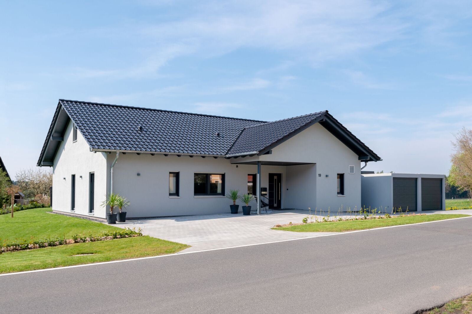 Modernes FingerHaus NIVO 130 mit Satteldach, heller Fassade, überdachtem Eingang und angebauter Doppelgarage, aufgenommen aus Straßenperspektive bei sonnigem Wetter.