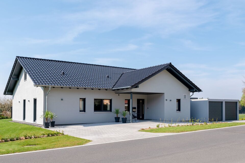 Modernes FingerHaus NIVO 130 mit Satteldach, heller Fassade, überdachtem Eingang und angebauter Doppelgarage, aufgenommen aus Straßenperspektive bei sonnigem Wetter.
