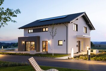 Außenansicht des FingerHaus-Musterhauses ARTIS im Schwarzwald bei Dämmerung mit moderner Architektur, Satteldach, beleuchtetem Garten und großzügigem Grundstück.