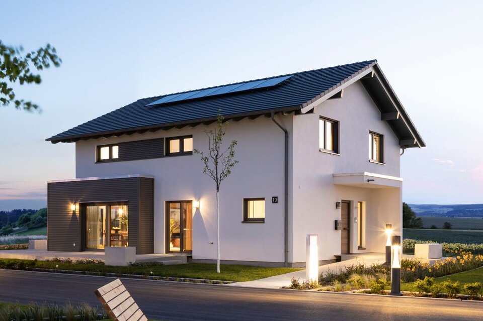 Außenansicht des FingerHaus-Musterhauses ARTIS im Schwarzwald bei Dämmerung mit moderner Architektur, Satteldach, beleuchtetem Garten und großzügigem Grundstück.