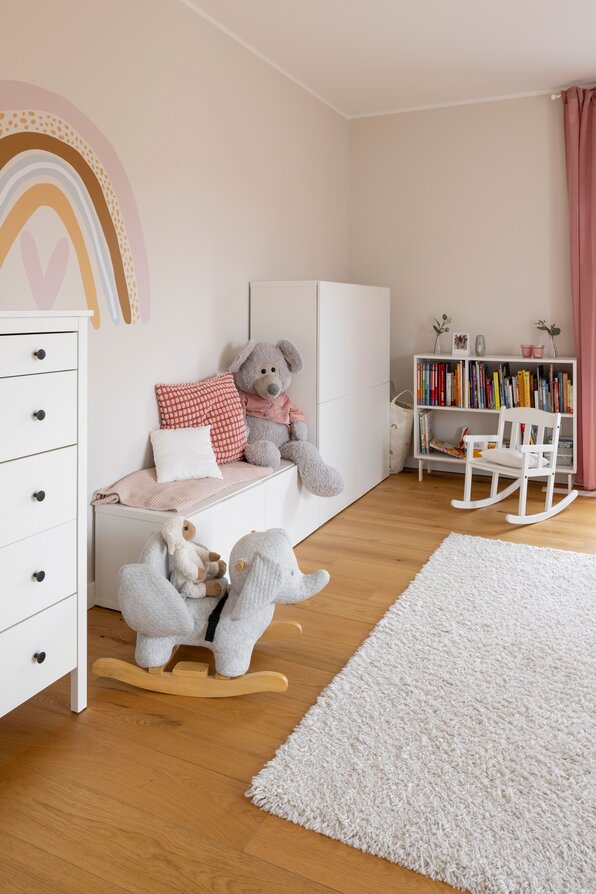 Helles Kinderzimmer mit Holzfußboden, Spielzeug, bunter Wandgestaltung und gemütlicher Spielecke.