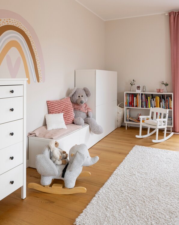 Helles Kinderzimmer mit Holzfußboden, Spielzeug, bunter Wandgestaltung und gemütlicher Spielecke.