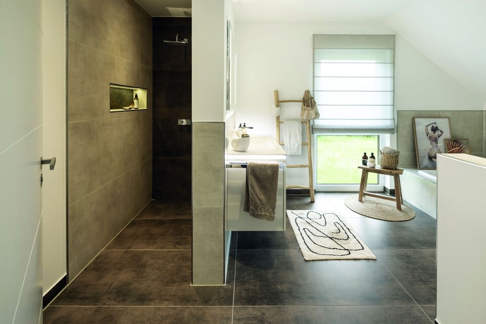 Modernes Badezimmer mit begehbarer Dusche, dunklen Boden- und Wandfliesen sowie heller Badewanne unter dem Fenster. Handtuchhalter, Teppich und Dekoration ergänzen das Design.