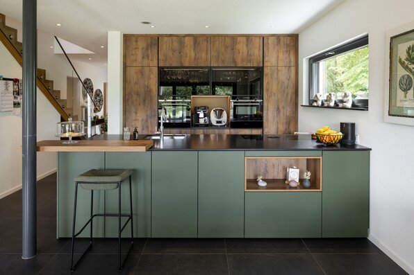 Moderne Küche mit grünem Küchenblock, Holzfronten, schwarzer Arbeitsplatte und integriertem Barplatz.