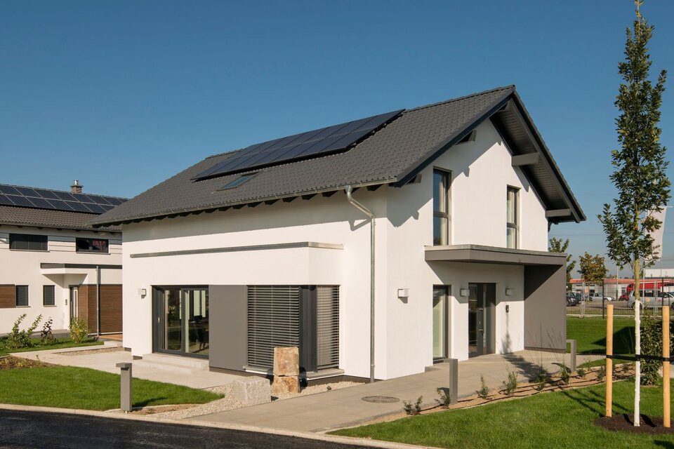 FingerHaus NEO Musterhaus in Günzburg bei strahlendem Sonnenschein mit moderner Fassade, dunklem Dach und integrierter Photovoltaikanlage.