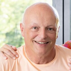 Ein Paar sitzt lächelnd am Küchentresen in einem frei geplanten FingerHaus. Auf dem Tisch stehen Kaffeetassen, eine Obstschale und eine Blumendekoration.