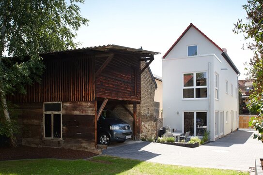 Modernes FingerHaus mit Satteldach und heller Fassade, kombiniert mit einem alten Holzschuppen im Garten.