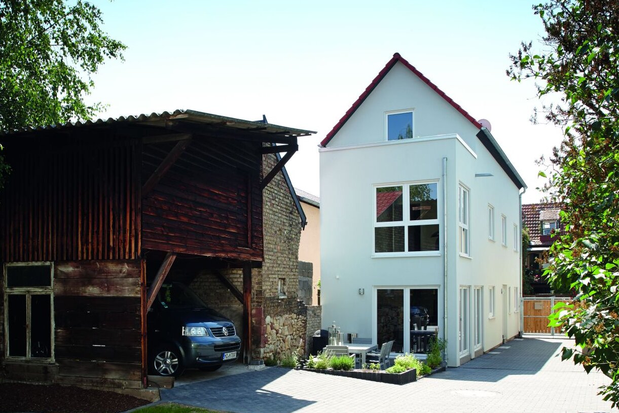 Modernes FingerHaus mit Satteldach und heller Fassade, kombiniert mit einem alten Holzschuppen im Garten.