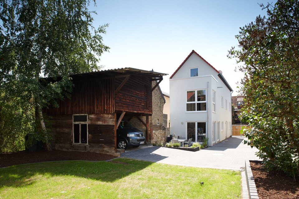 Modernes FingerHaus mit Satteldach und heller Fassade, kombiniert mit einem alten Holzschuppen im Garten.