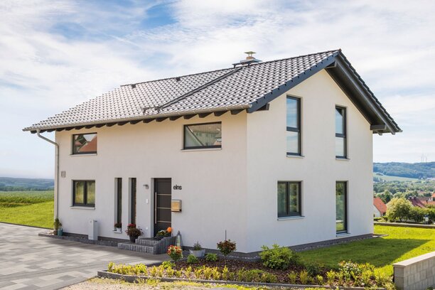 Außenansicht eines frei geplanten Finger-Hauses mit Satteldach, weißer Putzfassade, gepflasterter Einfahrt und angelegtem Vorgarten.