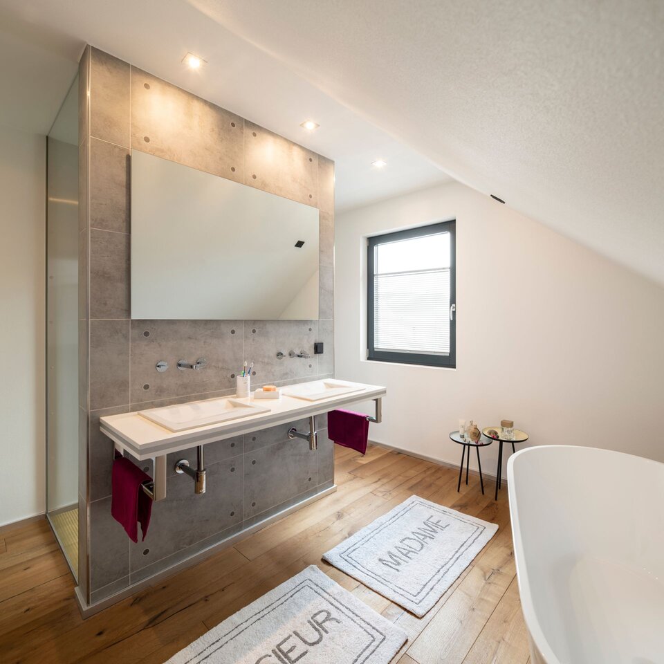 Modernes Badezimmer unter dem Dach mit großem Spiegel, Waschbereich und Holzfußboden.