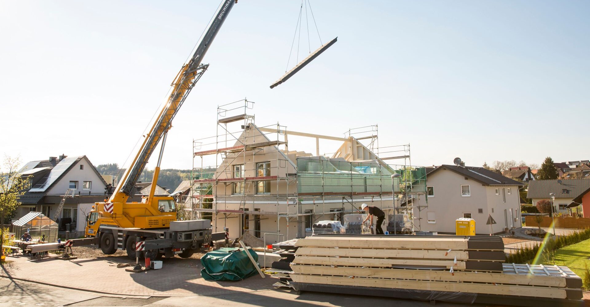 Montage eines Finger-Hauses mit Kran und Gerüst auf einer Baustelle bei Tageslicht.