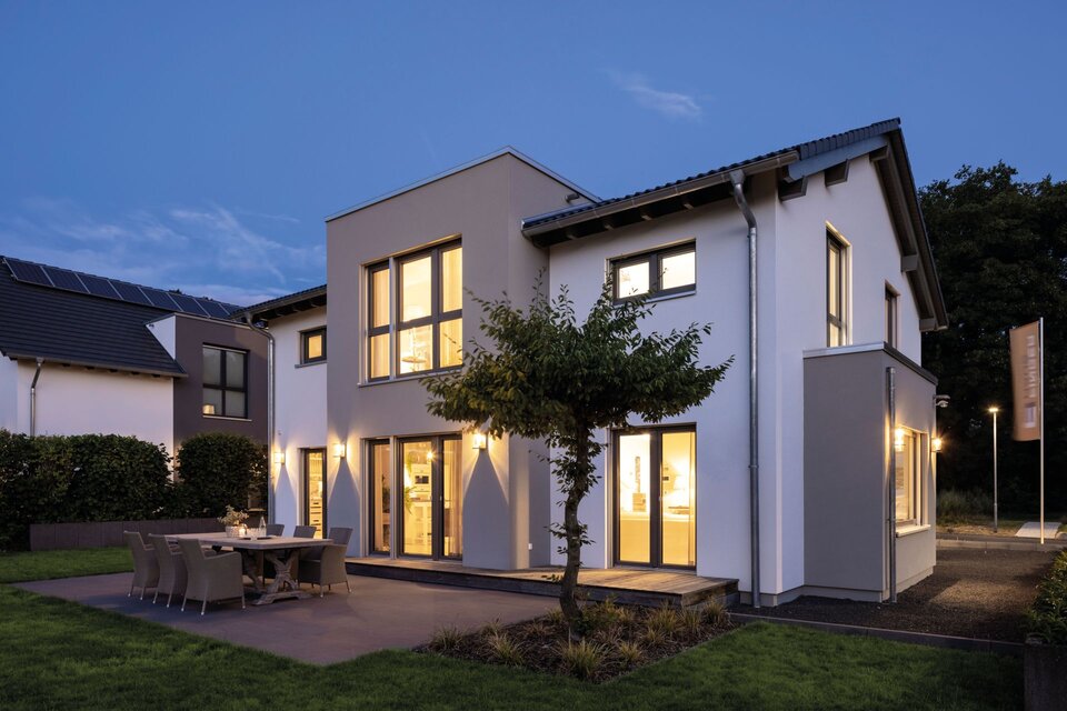 Modernes FingerHaus SENTO 503 Musterhaus in Bad Vilbel bei Abenddämmerung mit beleuchteter Fassade und Terrasse.