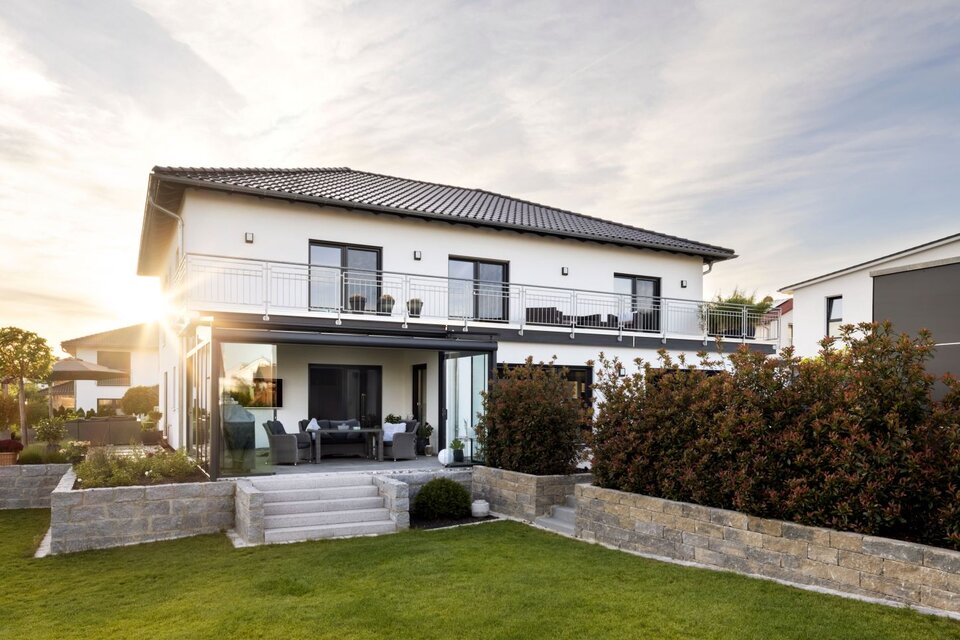 Zweistöckiges modernes FingerHaus mit großem Garten und Terrasse im Abendlicht, die Sonne scheint durch die Glasveranda.