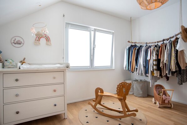 Helles Kinderzimmer in einem frei geplanten FingerHaus mit Holzschaukelpferd, Wickelkommode und offener Kleiderstange.