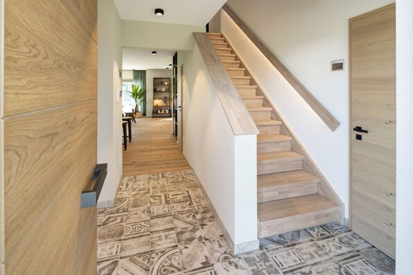 Eingangsbereich im FingerHaus ARTIS 400 Musterhaus Schwarzwald mit moderner Holztreppe, stilvollem Fliesenboden und Blick in den offenen Wohnbereich.