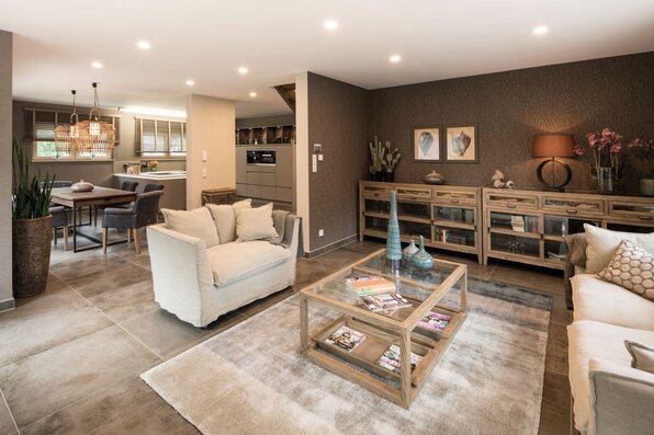 Offener Wohn-Essbereich im FingerHaus-Musterhaus MEDLEY in Fellbach mit gemütlicher Sofaecke, Essplatz, moderner Küche im Hintergrund und harmonischer, warmer Innenraumgestaltung.