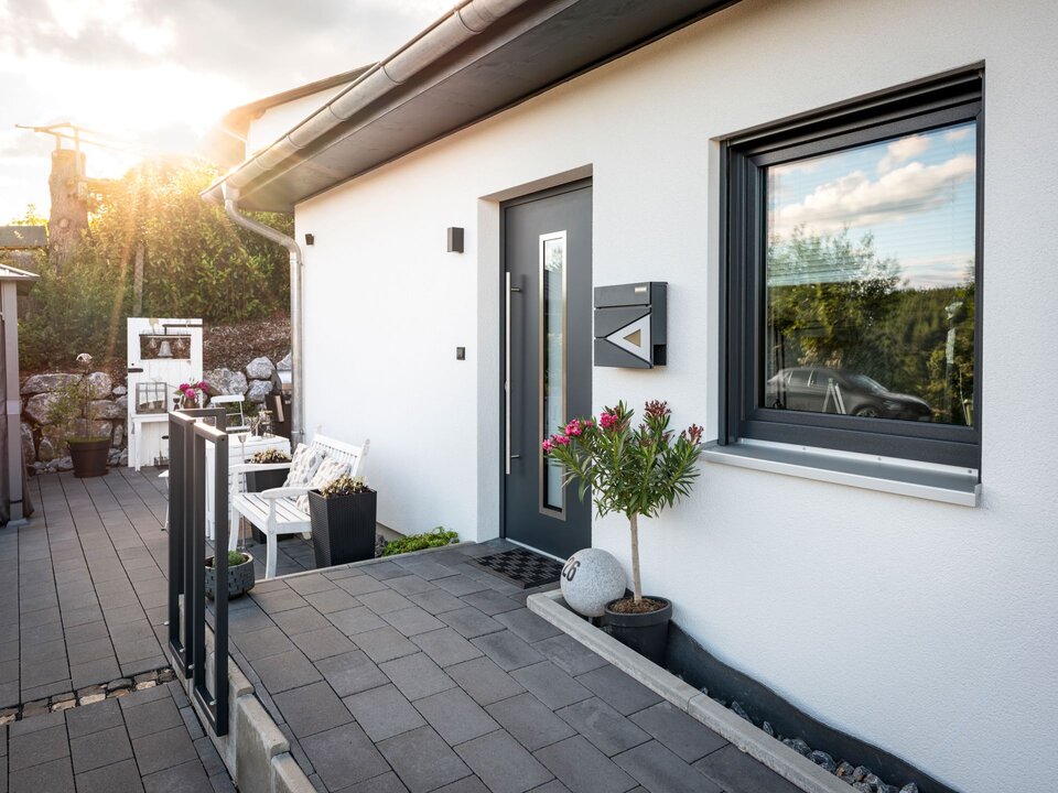 Eingangsbereich des Kundenhauses NIVO 80 mit Haustür, Briefkasten und gepflastertem Zugangsweg in der Abendsonne.