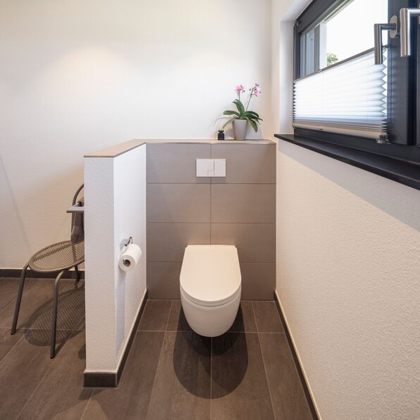 Badezimmer mit wandhängendem WC, Fenster und halbhoher Trennwand.