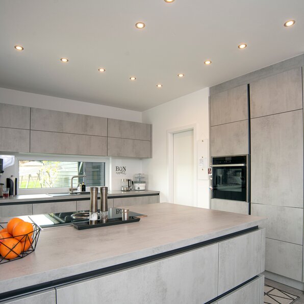 Moderne Küche mit großer Kücheninsel, Einbauherd, Ober- und Unterschränken sowie mehreren Decken-Einbaustrahlern