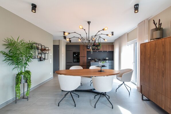 Moderner Essbereich mit angrenzender offener Küche im FingerHaus Musterhaus TALO in Babenhausen. Großer Holztisch mit weißen Stühlen, auffällige Designerlampe und elegante schwarze Küchenzeile im Hintergrund.