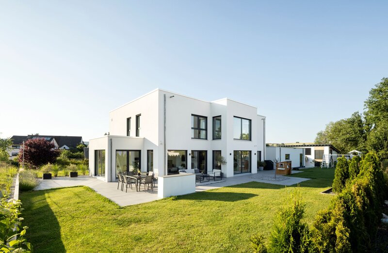Moderne Außenansicht eines frei geplanten FingerHaus im Bauhaus-Stil. Kubische Architektur mit weißer Fassade, großen Fensterfronten und weitläufiger Terrasse im Garten.