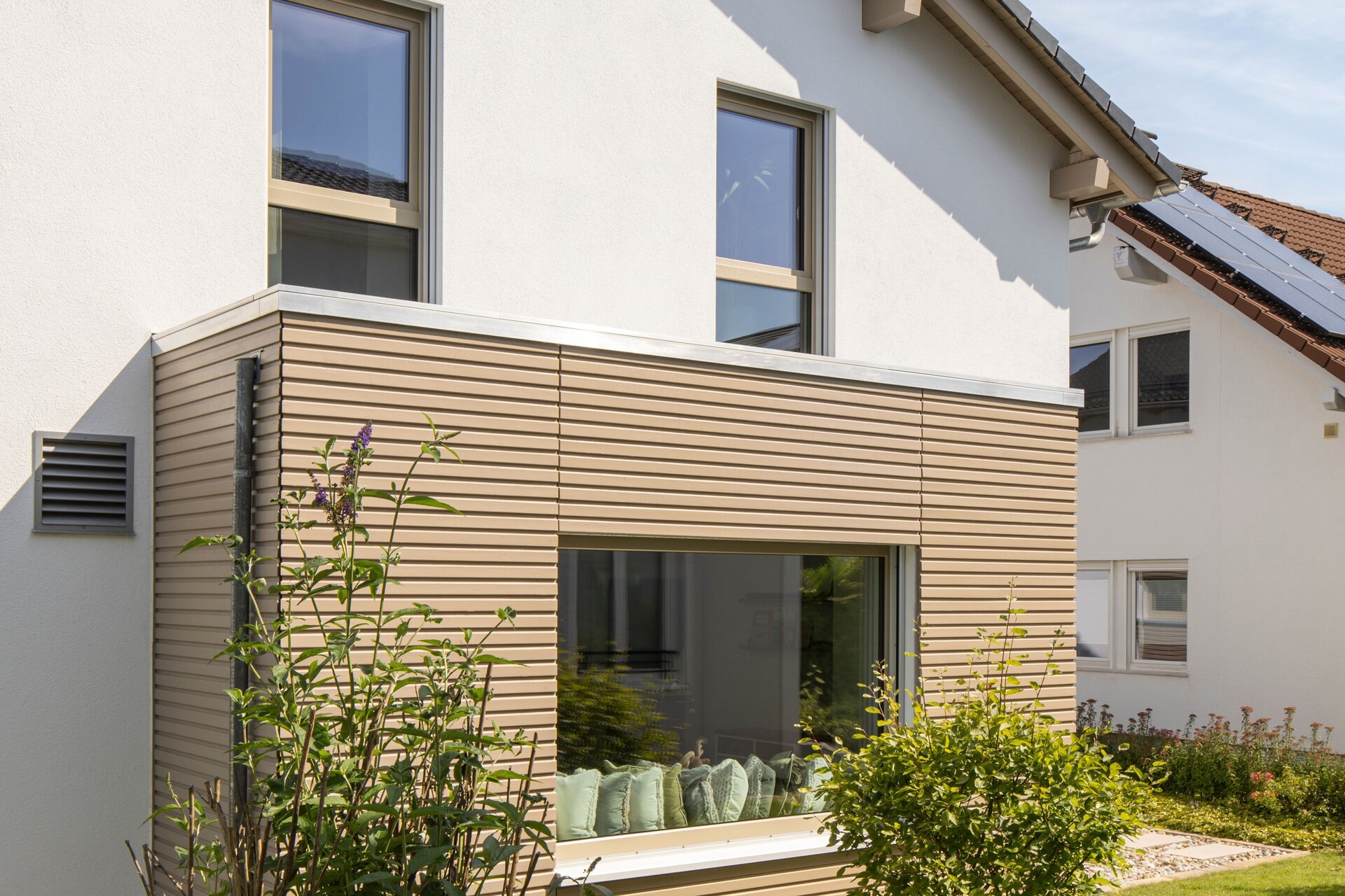 Außenansicht des Musterhauses MEDLEY 300 B in Poing mit hellem Putz, großem Wintergarten und gepflegter Gartenanlage.