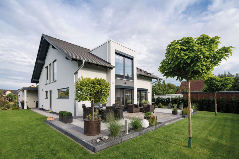 Frei geplantes zweigeschossiges FingerHaus mit heller Fassade, großem Terrassenbereich, modernen Gartenmöbeln, gepflegtem Rasen und formgeschnittenen Bäumen.