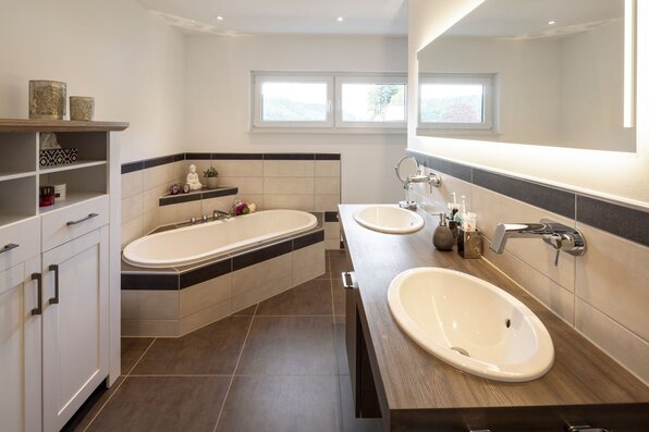 Modernes Badezimmer in einem FingerHaus mit Eckbadewanne, Doppelwaschbecken auf Holzkonsole und großem Spiegel.