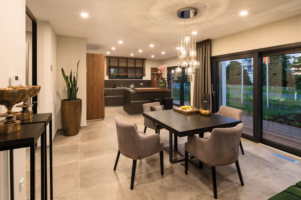 Moderner Essbereich mit dunklem Tisch, vier gepolsterten Stühlen, offener Küche im Hintergrund und großen Glas-Schiebetüren zum Garten