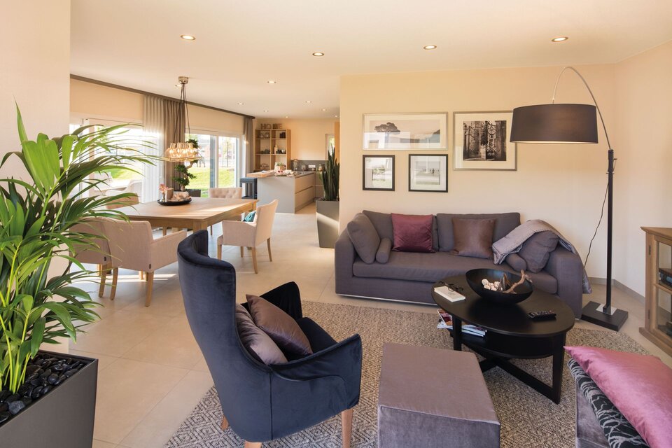 Helles Wohnzimmer im FingerHaus NEO Musterhaus Günzburg mit moderner Einrichtung, gemütlicher Sitzgruppe und Blick in den Ess- und Küchenbereich.