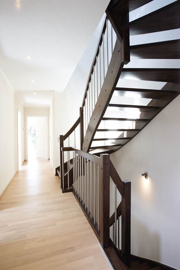Dunkle Holztreppe mit Metallgeländer in einem hellen Flur eines modernen FingerHaus-Hauses.