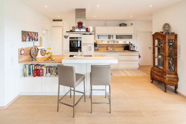 Moderne Küche in einem frei geplanten FingerHaus mit Kochinsel, integrierten Geräten, hellen Fronten, Barhockern und stilvoller Kombination aus moderner und klassischer Einrichtung.