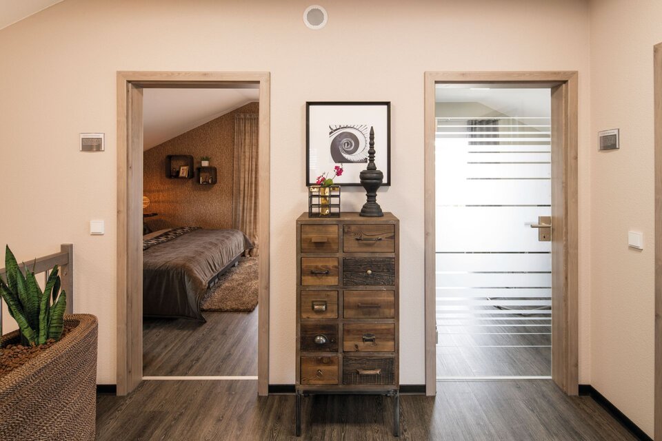 Flur im Musterhaus UNO Leipzig mit Holzboden, Kommode im Vintage-Stil und Blick ins Schlafzimmer.