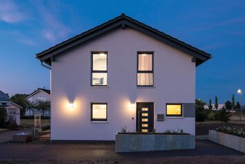 FingerHaus UNO 2.0 Musterhaus in Leipzig bei Abenddämmerung mit beleuchteter Fassade.