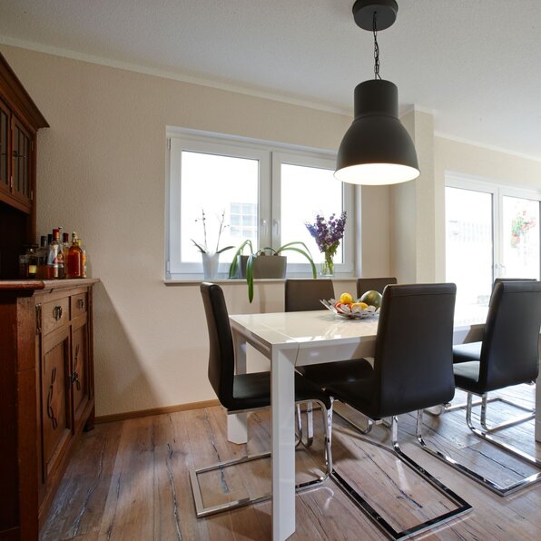 Essbereich mit modernem Tisch und schwarzen Stühlen, angrenzend an das Wohnzimmer mit Sofa in einem frei geplanten FingerHaus.