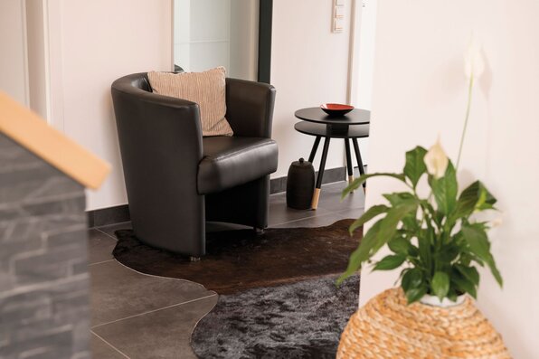 Gemütliche Sitz- und Deko-Ecke im Flur eines modernen FingerHaus-Hauses mit Ledersessel, Beistelltisch, Teppich und Zimmerpflanze.