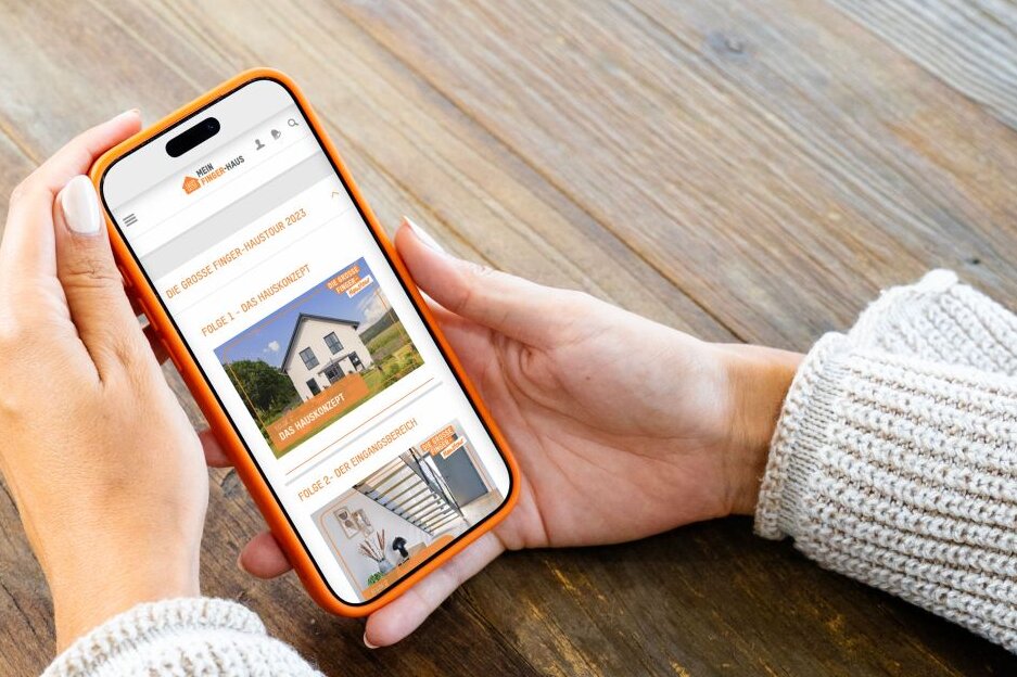 Person hält ein Smartphone mit dem FingerHaus Serviceportal in den Händen. Auf dem Display sind Informationen zur großen Finger-Haustour dargestellt.