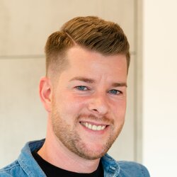 Ein Mann hält ein Baby im Arm und lächelt in einem hellen Wohnraum des FingerHaus NIVO 130.