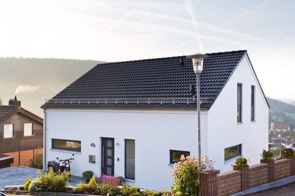 Modernes Einfamilienhaus von FingerHaus mit weißer Fassade, dunklem Satteldach, klaren Linien und Vorgarten, gelegen in Hanglage mit Blick ins Tal.