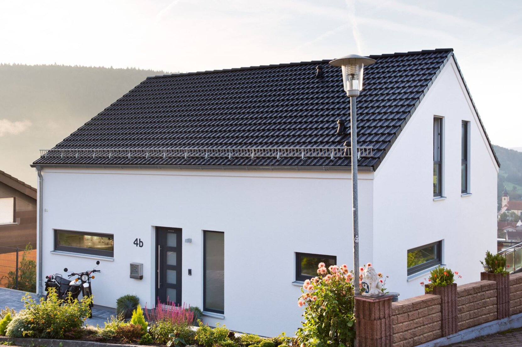 Modernes Einfamilienhaus von FingerHaus mit weißer Fassade, dunklem Satteldach, klaren Linien und Vorgarten, gelegen in Hanglage mit Blick ins Tal.