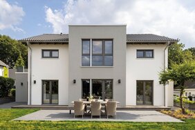 Außenansicht des FingerHaus-Musterhauses SENTO in Bad Vilbel mit moderner, symmetrischer Architektur, heller Putzfassade, großer Terrasse und gepflegtem Garten.